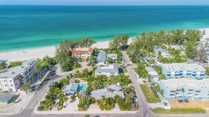 An aerial view of a coastal resort with beachfront properties, roads, and greenery.