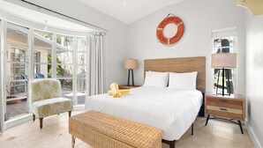 A bedroom with a large bed, a wicker bench, a chair, a bedside table, and a lamp.