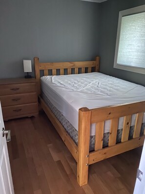 A bedroom with a wooden bed, a nightstand, and a window with blinds. - Private 4 Season Waterfront Cottage - 2 hrs from TO -Great Swimming / FAST WI-FI (Minden)