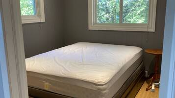 A bedroom with a bed, two windows, a small table, and a wooden floor.
