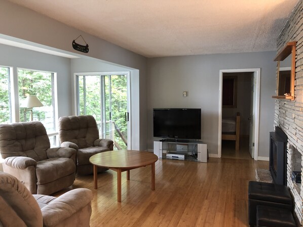 A living room with a flat-screen TV, two armchairs, a coffee table, and a fireplace.