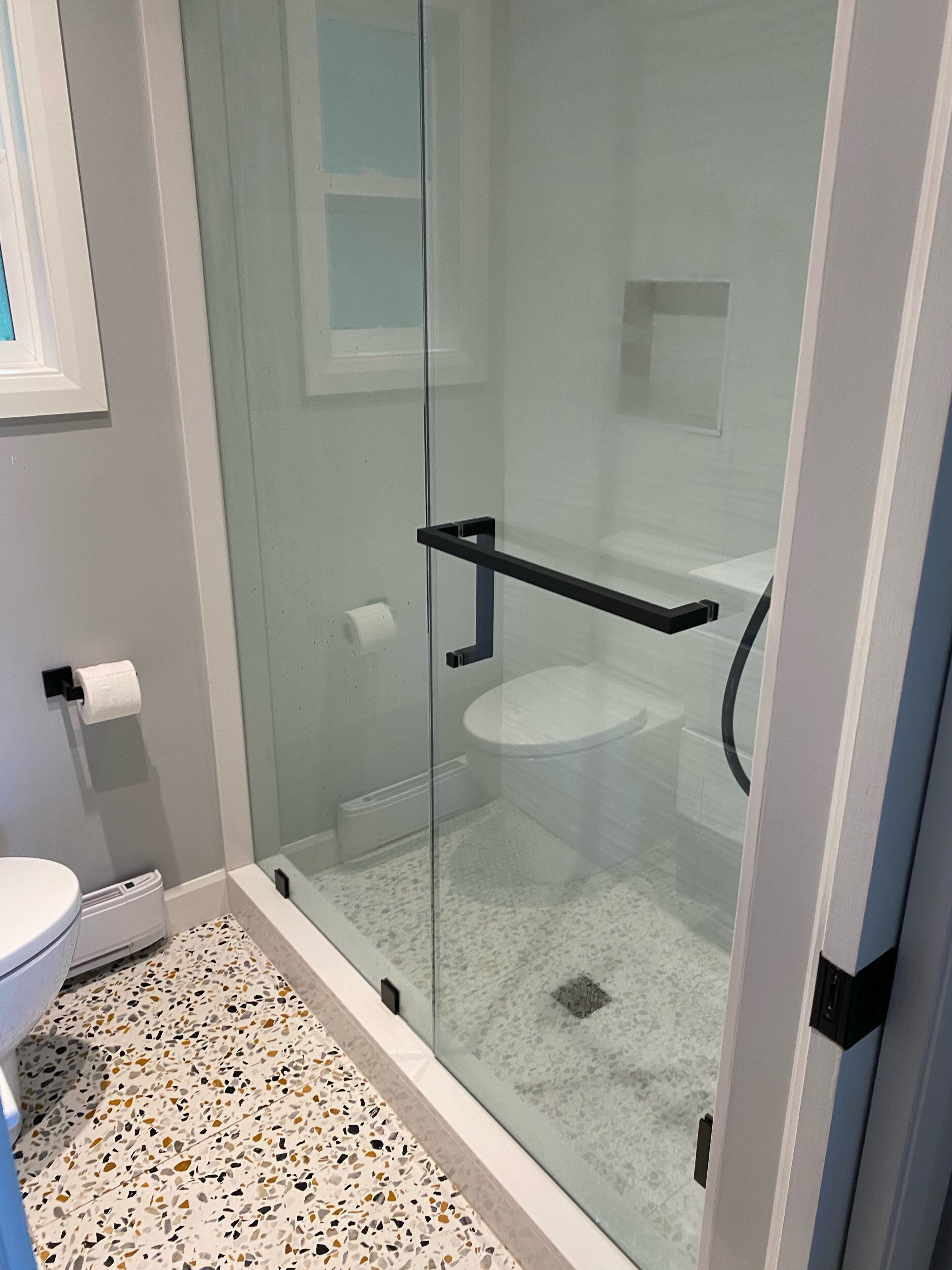 A modern bathroom with a glass-enclosed shower, a white toilet, and a patterned floor.
