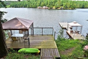 A wooden deck with a table and chairs, a covered seating area, and a green kayak. - Private 4 Season Waterfront Cottage - 2 hrs from TO -Great Swimming / FAST WI-FI (Minden)