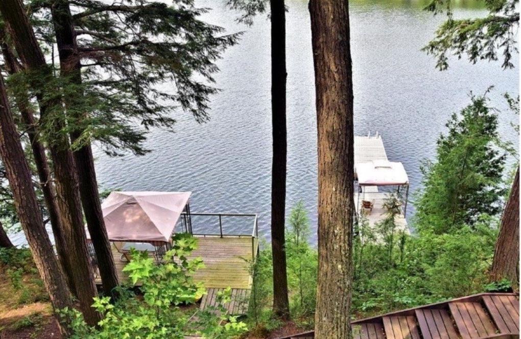 Una cabaña junto al lago con terraza y zona de estar cubierta al aire libre.