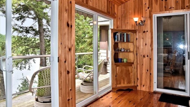 Un interior de madera con un cristalera corredera que da a una terraza, un estante pequeño y un sillón acolchado.