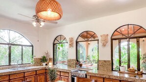 A kitchen with granite countertops, wooden cabinets, and a central island with a fruit bowl. - Private Jungle Palace with Designer Pool (Playa Hermosa)