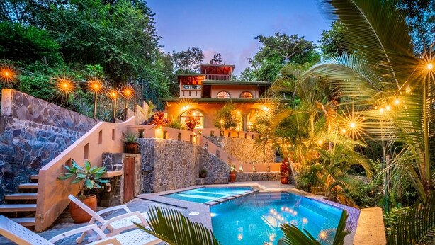 A pool area with lounge chairs, a stone wall, and a building with a balcony. - Private Jungle Palace with Designer Pool (Playa Hermosa)