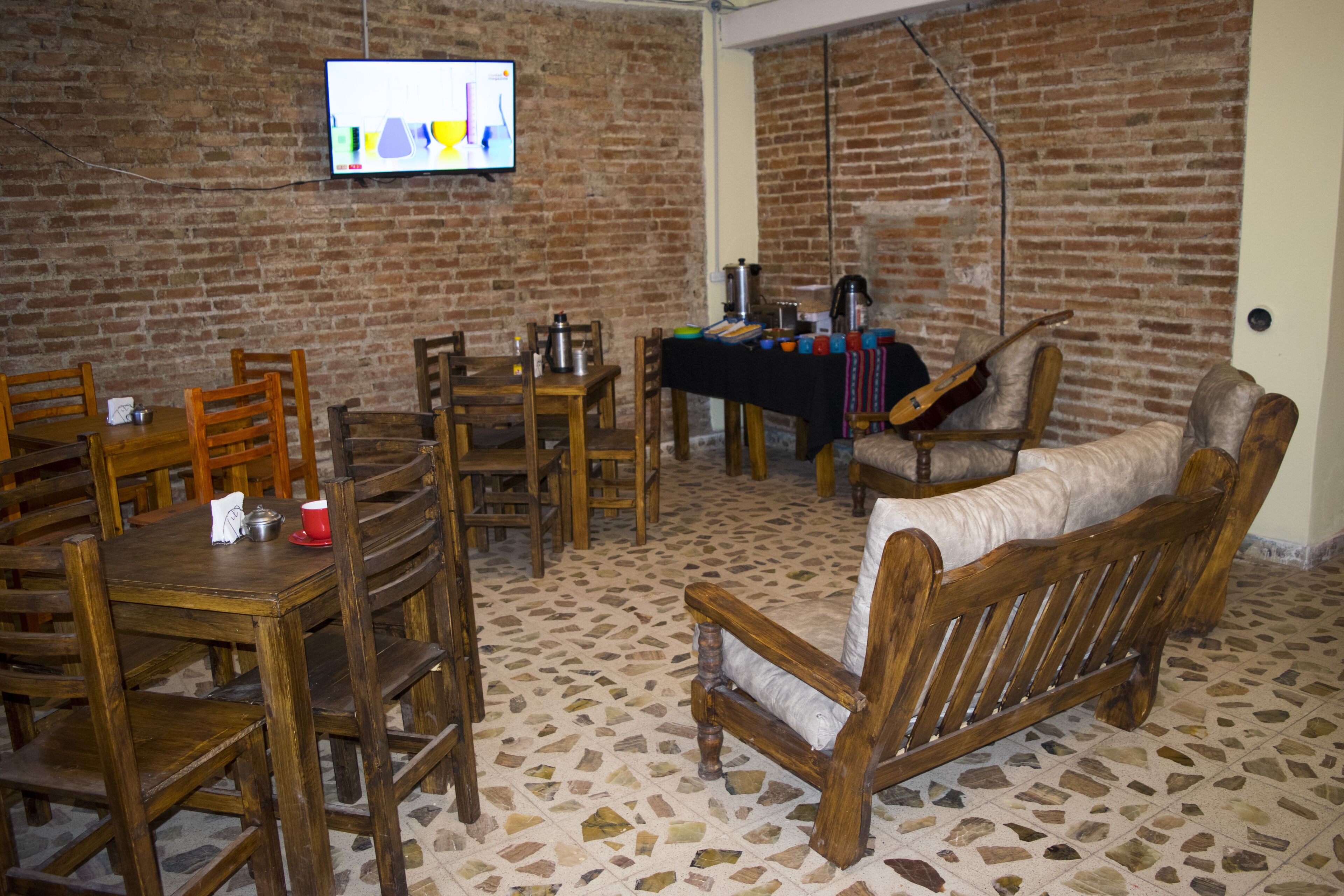 A room with a brick wall, a television mounted on it, wooden furniture including a table and chairs, and a sofa.