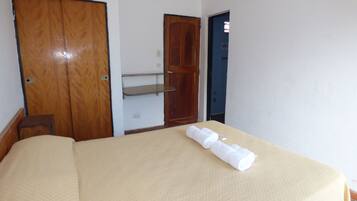 A hotel room with a bed, a wooden wardrobe, a shelf, and a door.