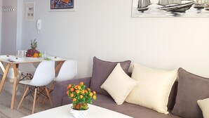 A living room with a white coffee table, a sofa, and a dining table with chairs. There is a painting of sailboats on the wall. - Apartment in front of the beach (Sarandë)