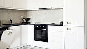 A modern kitchen with white cabinetry, a black oven, and a countertop with a coffee maker. - Apartment in front of the beach (Sarandë)