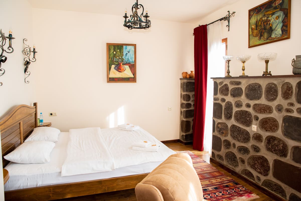 Un dormitorio con una cama de madera, ropa de cama blanca, una chimenea de piedra, un cuadro y una araña.