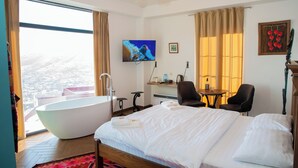 Una habitación de hotel moderna con una cama grande, una bañera, un escritorio y una televisión.