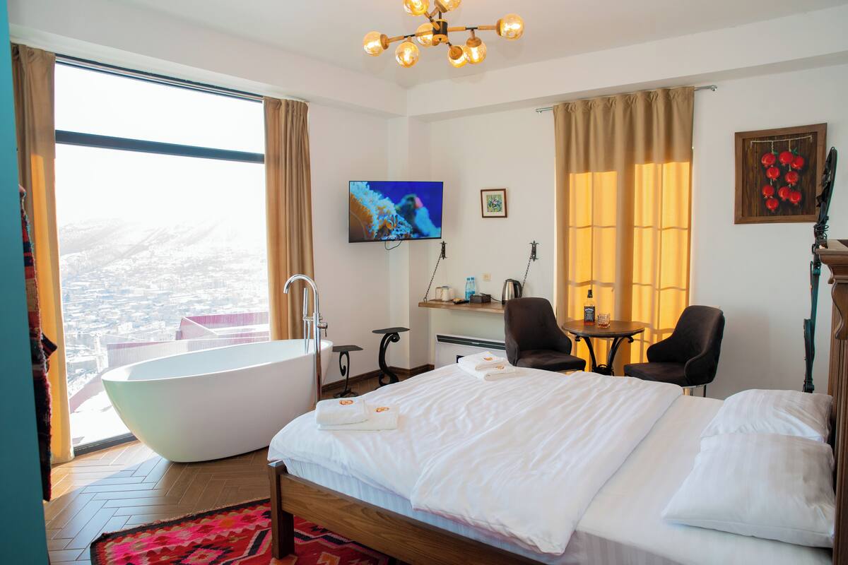 Una habitación de hotel moderna con una cama grande, una bañera, un escritorio y una televisión.