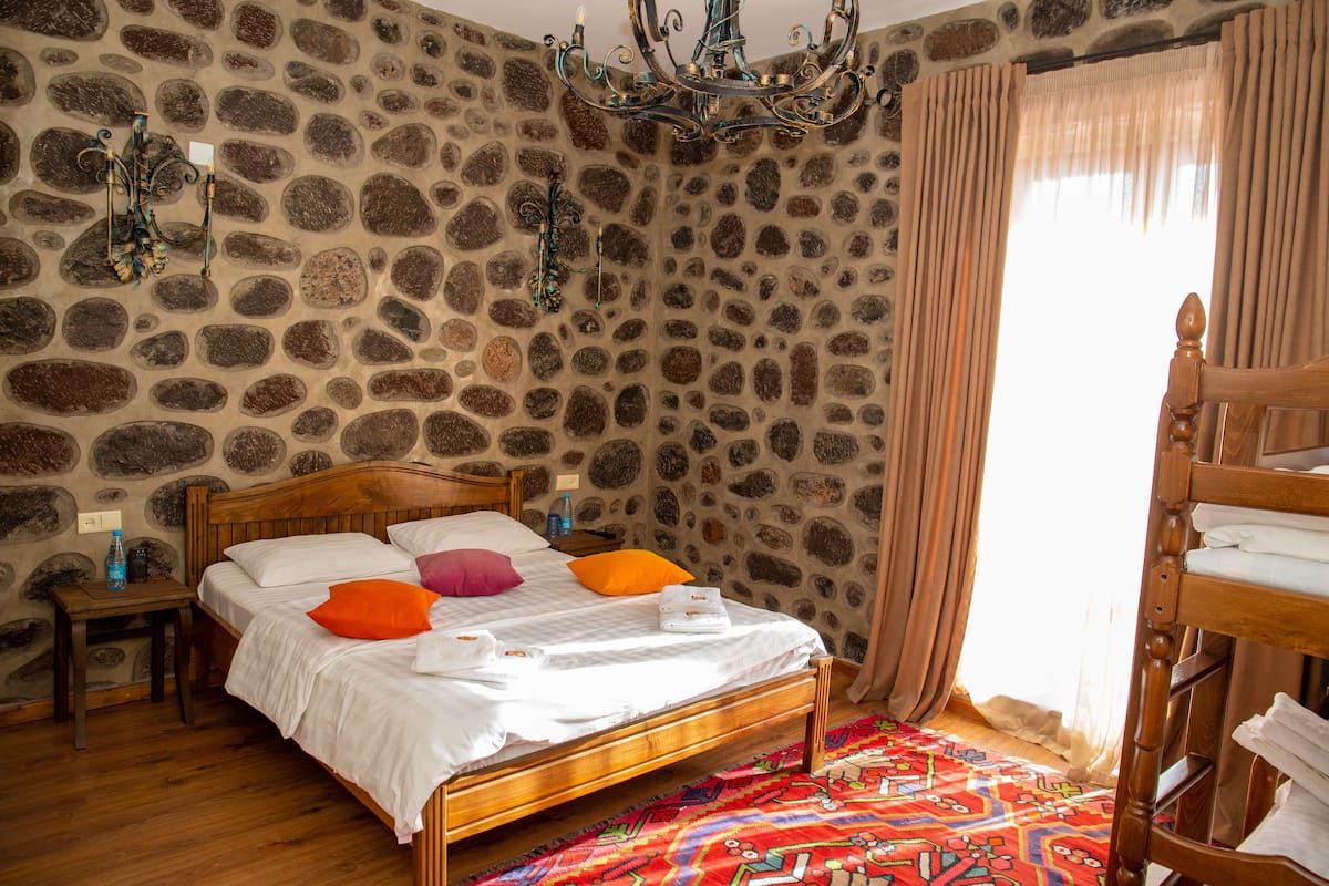 Un dormitorio con pared de piedra, cama de madera, alfombra colorida y litera de madera.