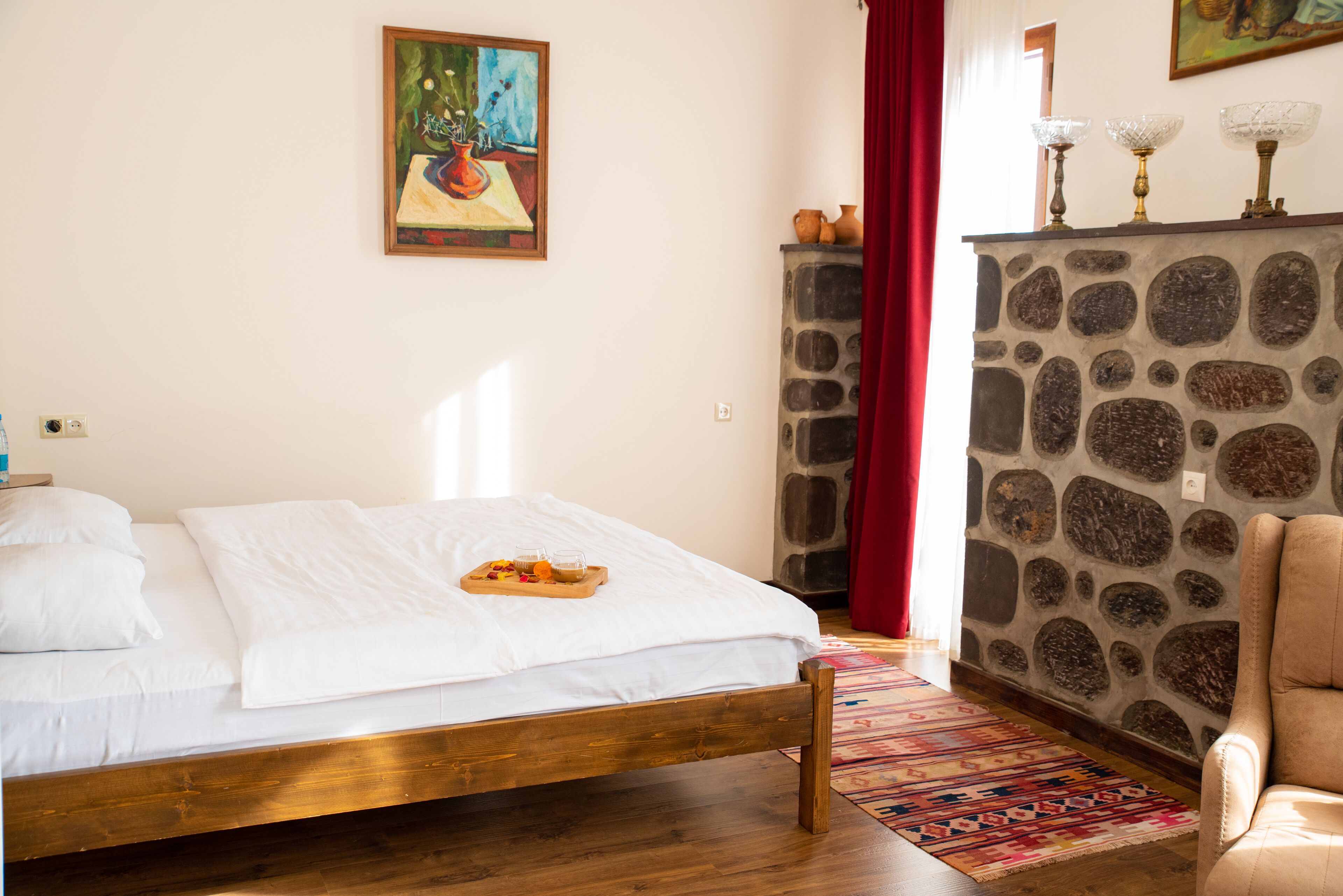 A bedroom with a wooden bed, a stone fireplace, a red curtain, and a painting on the wall.