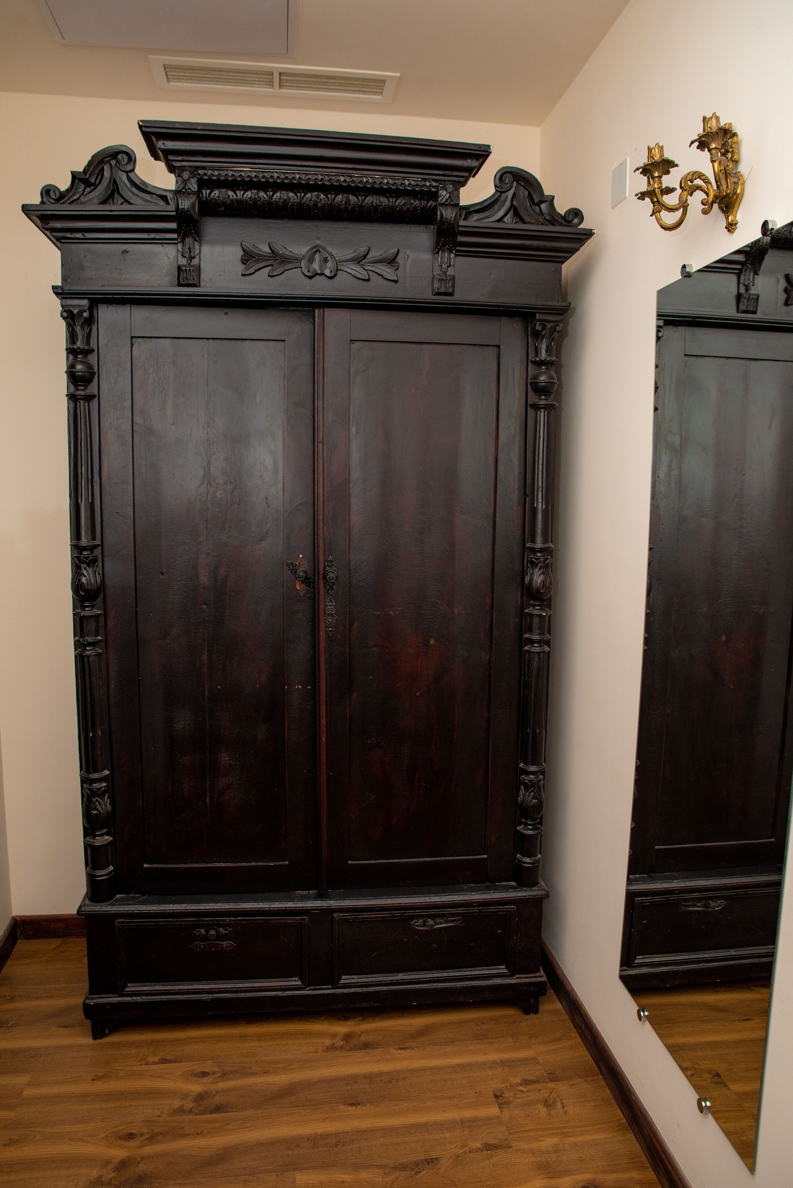 Une grande armoire en bois sombre, ornée de sculptures complexes, avec un miroir au-dessus.