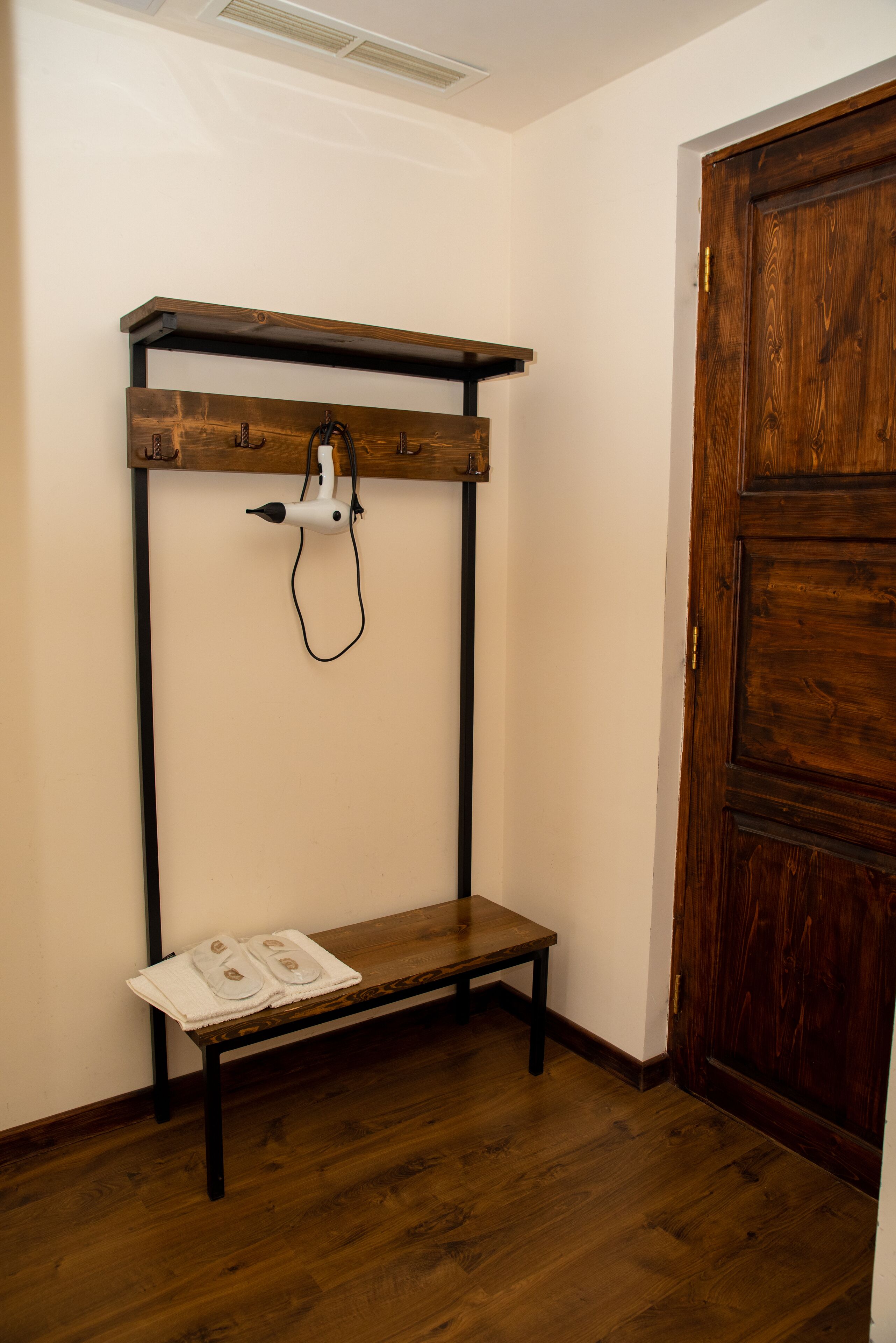 Una habitación con un banco de madera, un tendedero de pared y una puerta de madera.