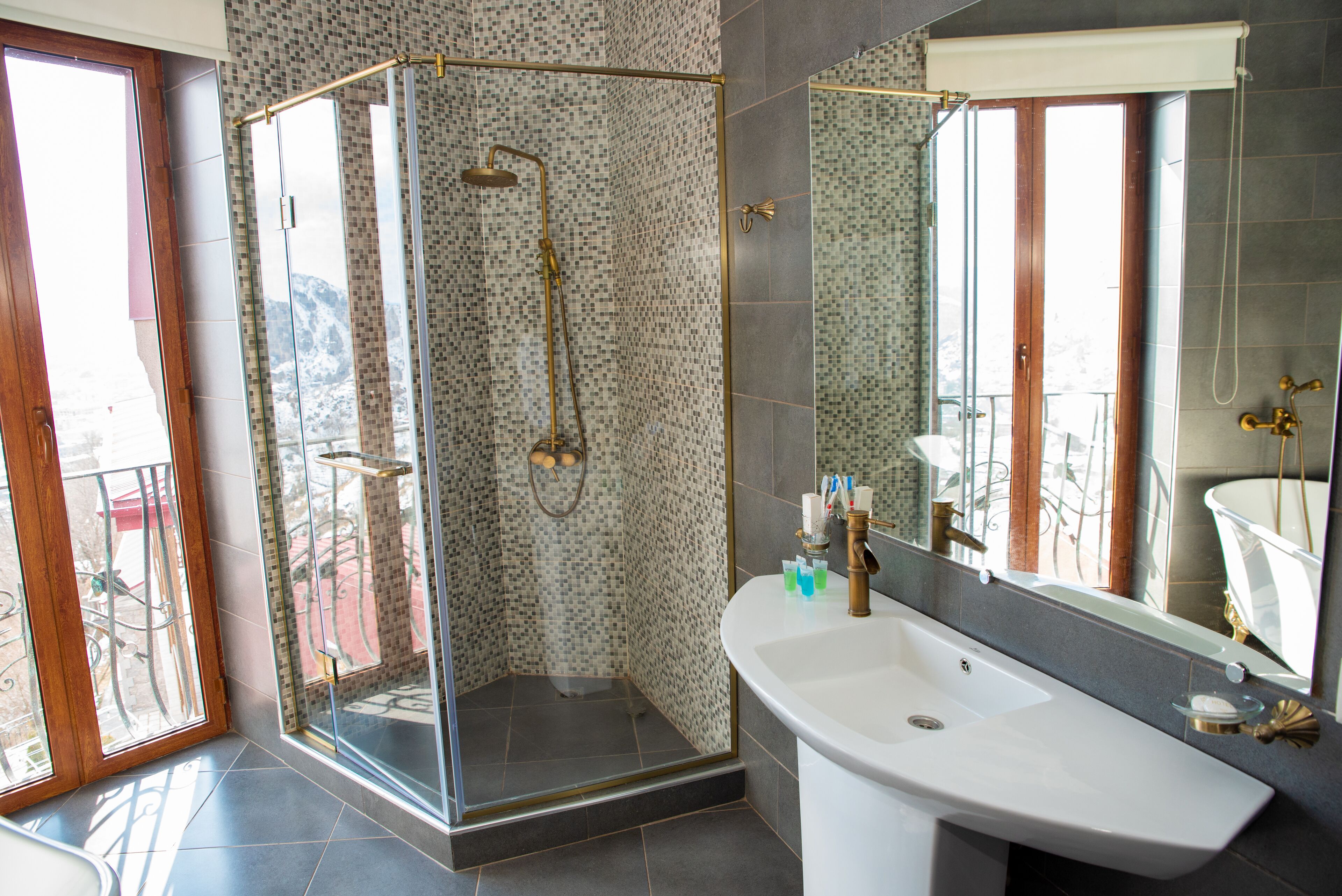 A modern bathroom with a glass-enclosed shower, a large sink, and a mirror reflecting a bathtub.