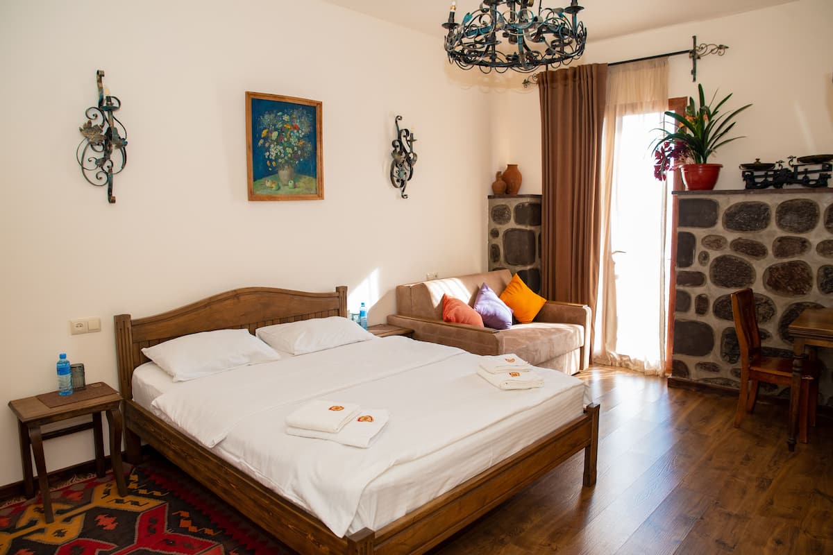 Un dormitorio ordenado con una cama de madera, una mesita auxiliar pequeña, un sofá con cojines de colores, una chimenea de piedra y un candelabro.