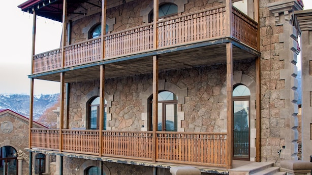 Un edificio de varios pisos con fachada de piedra, balcones y una escalera curva que lleva a la entrada.