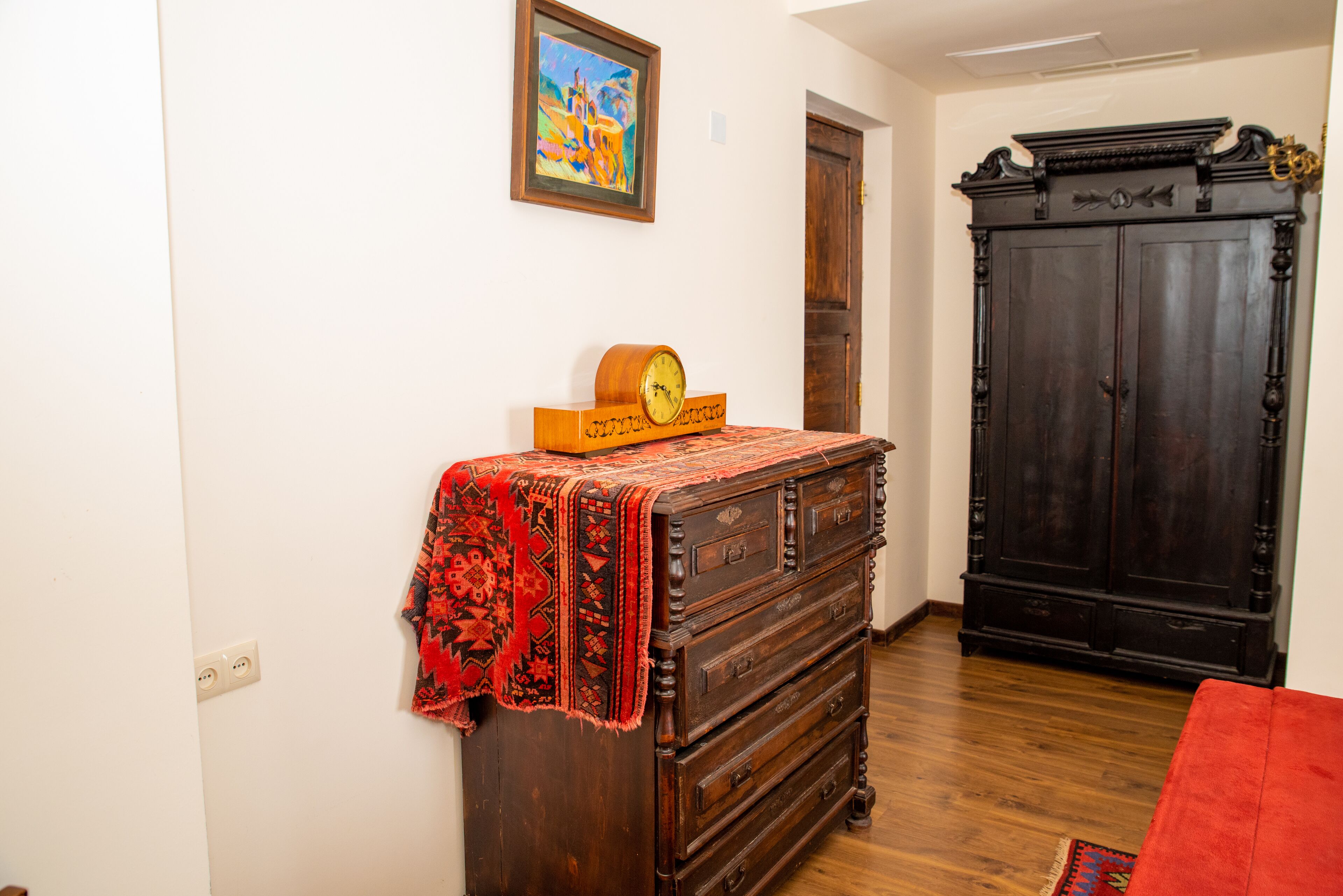 Una habitación con un aparador de madera, un mantel rojo estampado, un reloj y un armario de madera oscura.