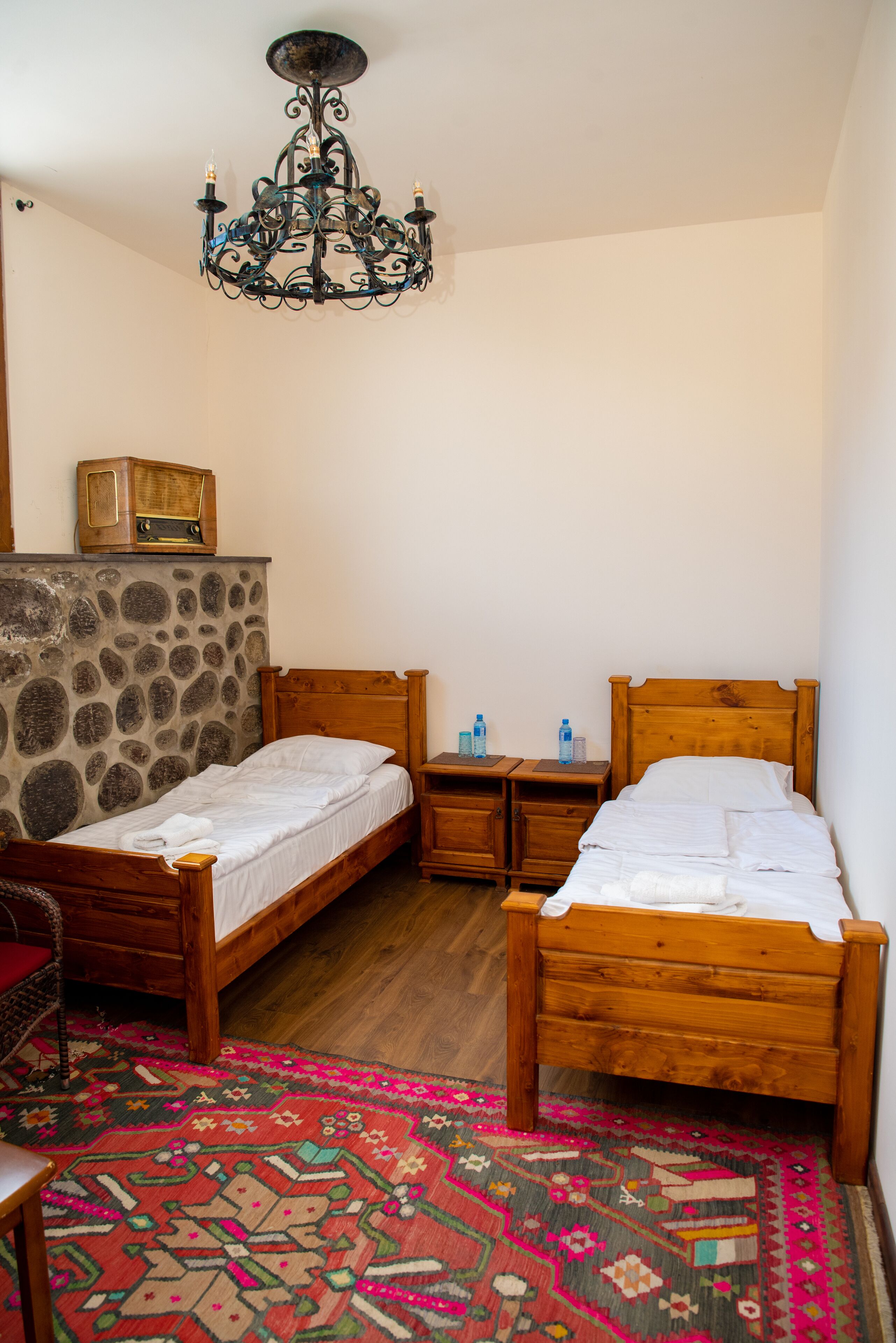 Una habitación con dos camas de madera, una pared de piedra, una araña y una alfombra estampada.