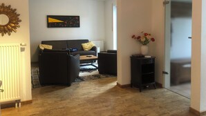 A living room with a sofa, a coffee table, and a side table with a vase of flowers. - Maison Euba am Zeisigwald (Euba)