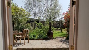 Blick durch eine offene Tür auf eine Steintreppe, einen Garten mit Bäumen und Gartenmöbeln.