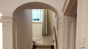 Eine Treppe mit beigefarbenen Teppichstufen und dunklen Holzstufen, die zu einer Zwischenebene mit einem Fenster und Vorhängen führt.