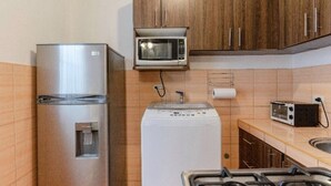 Una cucina compatta con frigorifero in acciaio inossidabile, forno a microonde, lavatrice e piano cottura a gas.