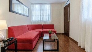Un soggiorno con un divano rosso, un tavolino in vetro, una lampada e una ventola a soffitto.