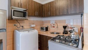 Una cucina compatta con pensili e basi in legno, un forno a microonde, un tostapane, un lavello e un piano cottura.