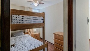 Un letto a castello con una ventola a soffitto, un comodino con una lampada e una cassettiera.