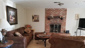Una sala de estar con chimenea de ladrillo, un sofá, una mesa de centro y un televisor.