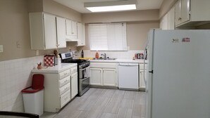 Una cocina compacta con armarios blancos, estufa, lavavajillas y refrigerador.
