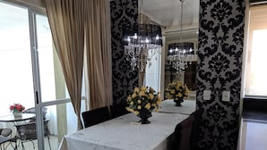 Un coin repas avec une table dressée pour quatre personnes, deux lustres et une vue à travers une porte vitrée.