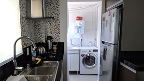 Une cuisine compacte équipée d’un évier, d’une cuisinière, d’une bouilloire et d’un lave-linge.