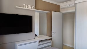Une chambre à coucher comprenant un lit, un téléviseur fixé au mur, une armoire et un miroir.