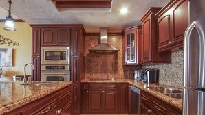 Una cocina con armarios de madera oscura, encimeras de granito, electrodomésticos de acero inoxidable y salpicadero de azulejos.