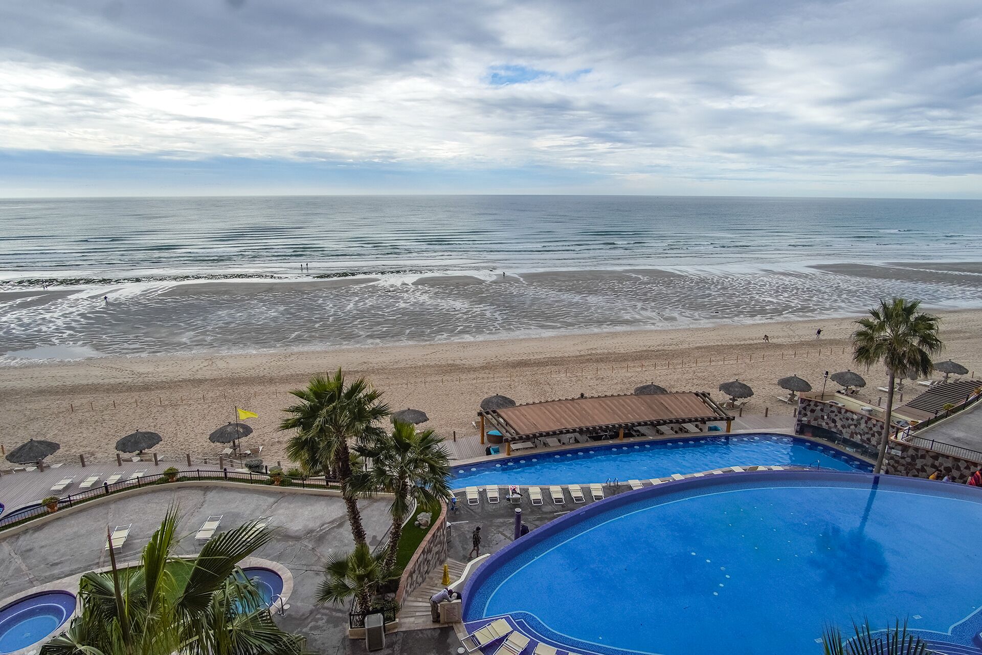 A resort with a large swimming pool, a beach area, and a view of the ocean.
