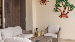 Un rincón exterior acogedor con mobiliario de mimbre y una mesa de madera, que incluye dos copas de vino y platos decorativos.