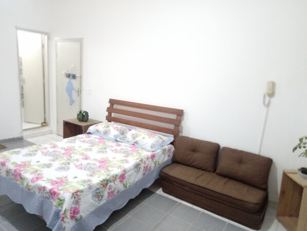 A bedroom with a bed, a brown sofa, a nightstand, and a wall-mounted phone. - Guarujá- suite with minibar, ceiling fan at 1, 7 km from Asturias beach (Guarujá)