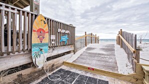 Een houten looppad dat naar een strand leidt, met een bewakingspost en een bord waarop een waterdiepte van 3 voet staat aangegeven.