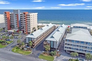 A coastal hotel with multiple buildings, including a prominent multi-story structure with orange accents, a modern building with a sloped roof, and a large glass facade building. - Ride the TIDE Beachside! 2Bd, 1B, Free Parking! Steps 2 Sand! 200 5 Star Reviews (Gulf Shores)