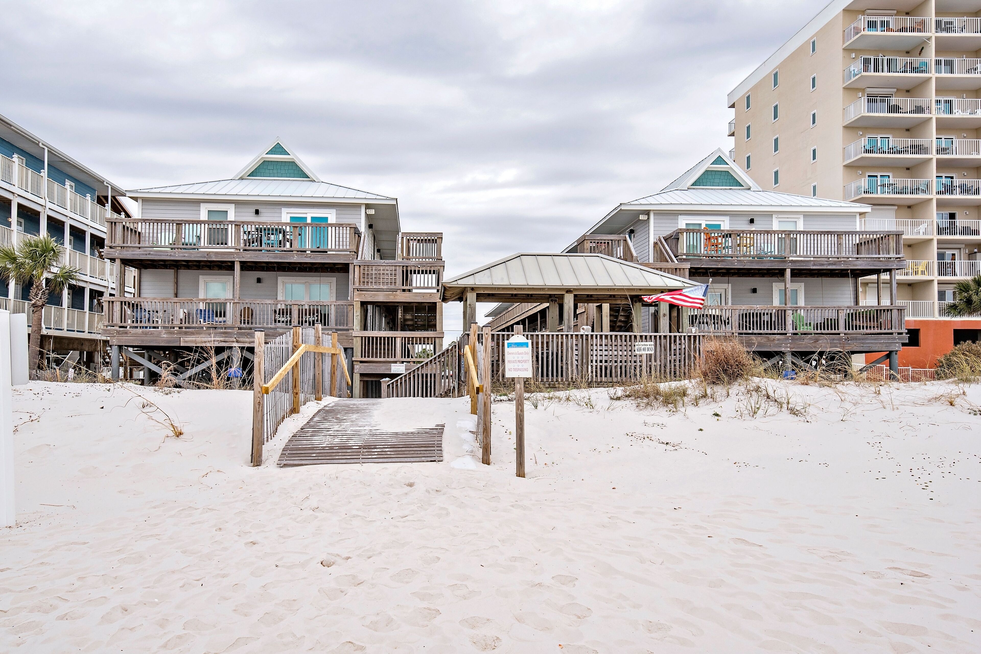 A beachfront hotel with multiple balconies, a covered walkway, and a sandy beach area.