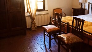 Una habitación con una mesa y sillas de madera, un radiador, una ventana con cortinas y una lámpara en el techo.