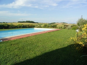 A rectangular swimming pool with a red border, surrounded by well-maintained grass and a clear sky.