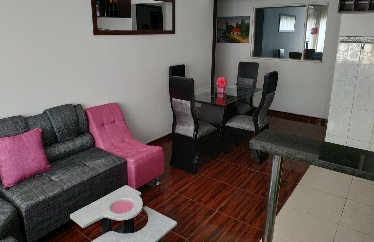 En moderne stue med en grå sofa, en pink skammel og et glasbord med stole.