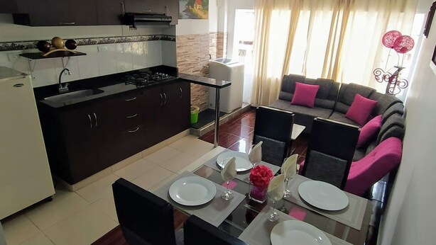 Uma cozinha moderna com armários escuros, fogão a gás e uma área de refeições com mesa de vidro e cadeiras pretas.